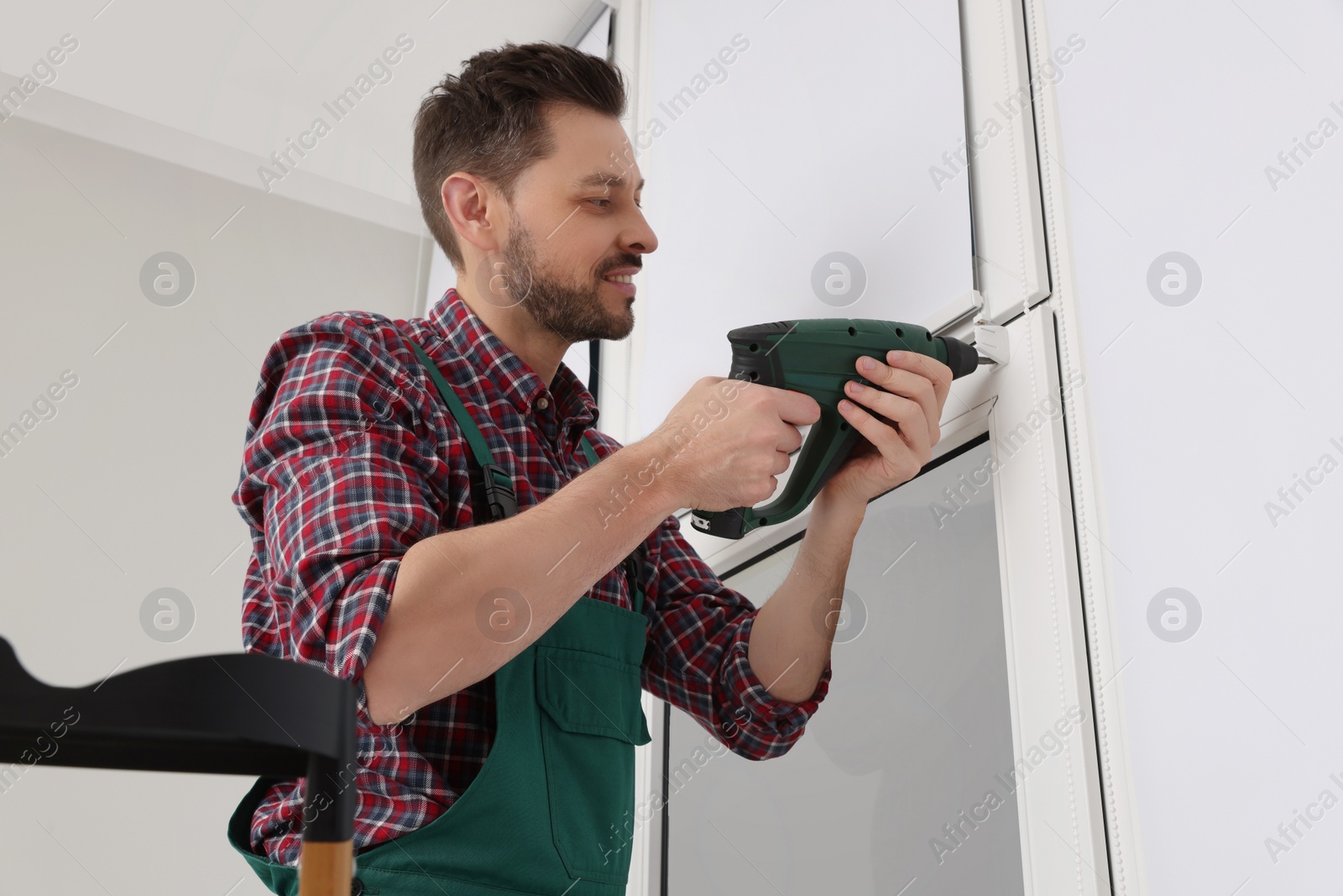 Photo of Worker in uniform installing roller window blind indoors