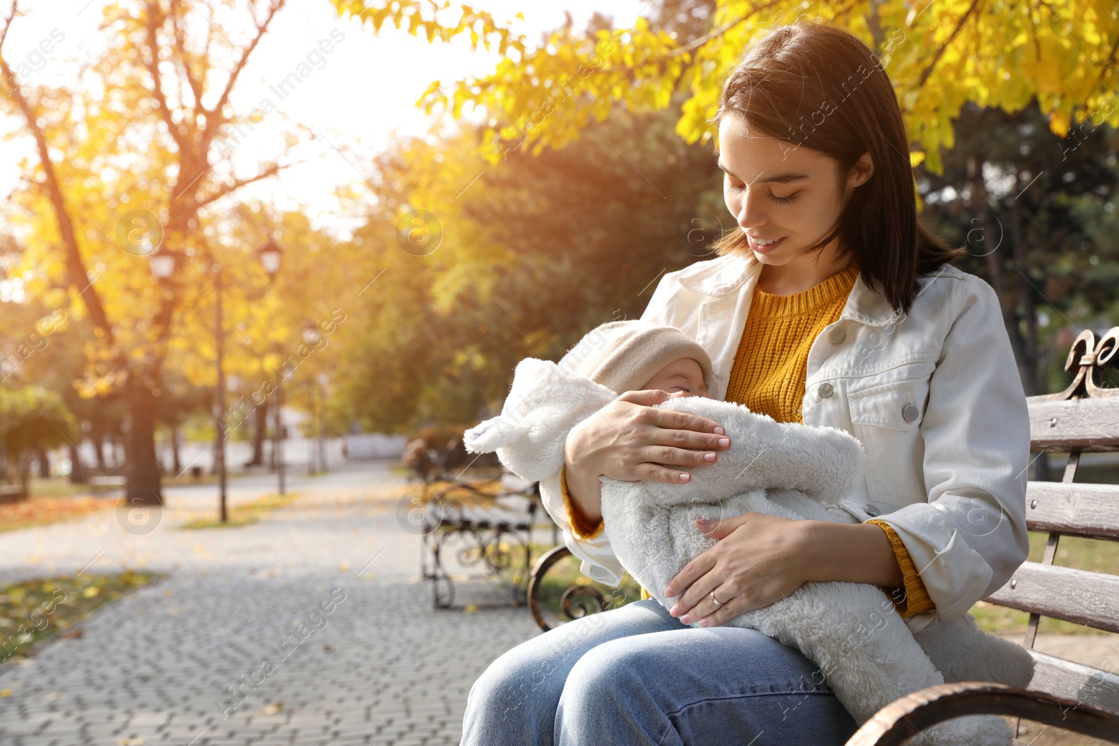 Photo of Happy mother with her sleeping baby son on bench in autumn park, space for text