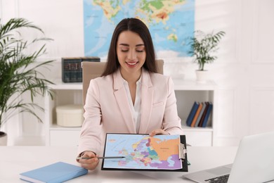 Photo of Happy manager showing map at desk in travel agency