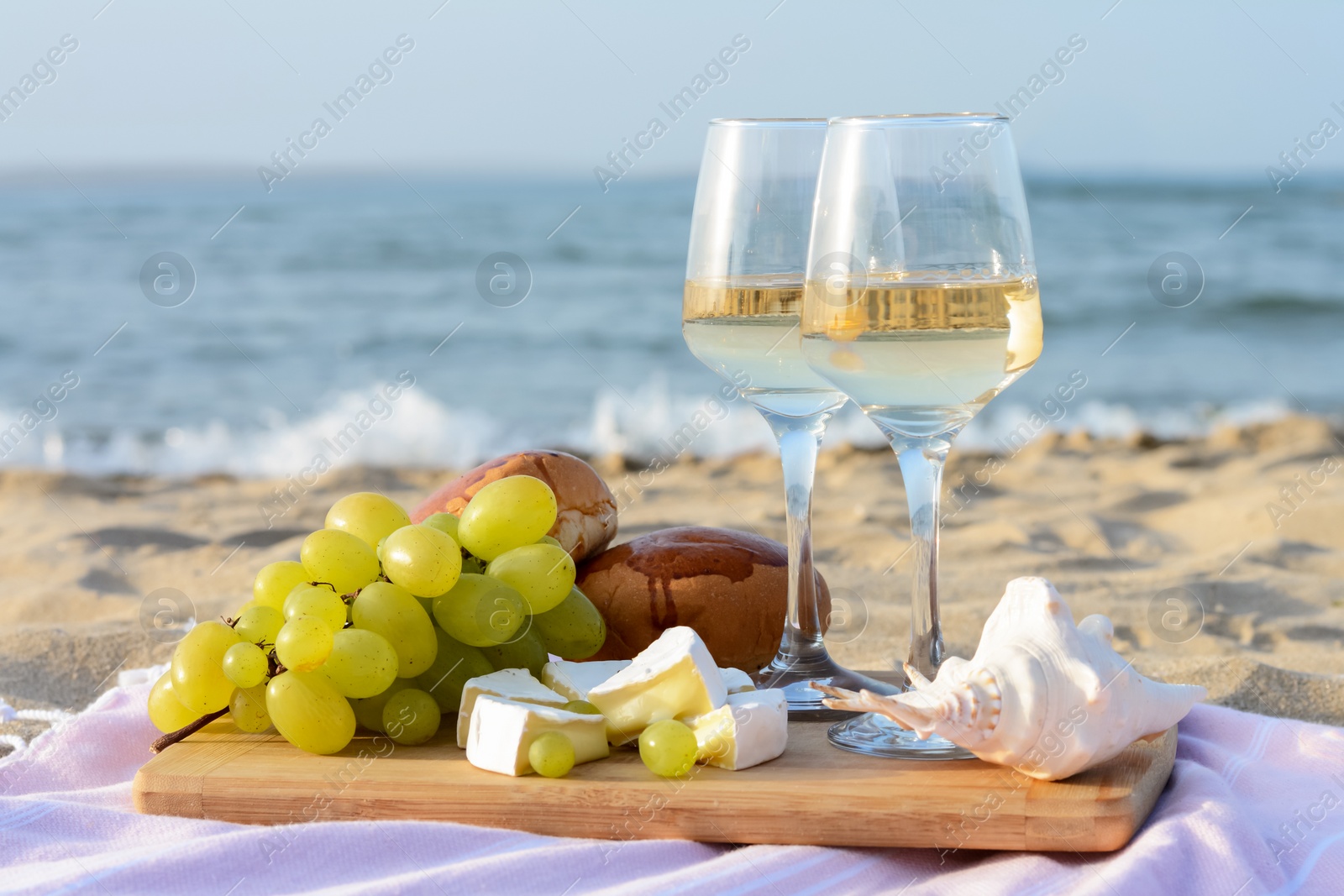 Photo of Glasses with white wine and snacks for beach picnic on sandy seashore