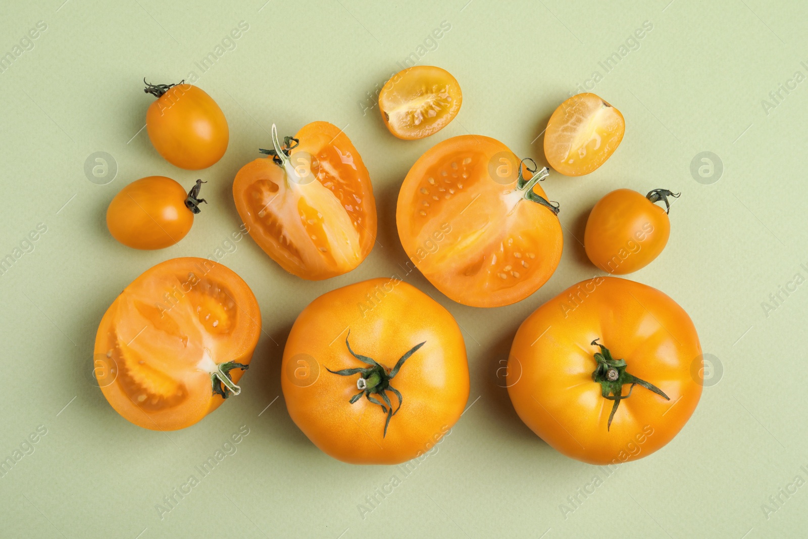 Photo of Cut and whole ripe yellow tomatoes on light green background, flat lay