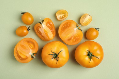 Cut and whole ripe yellow tomatoes on light green background, flat lay