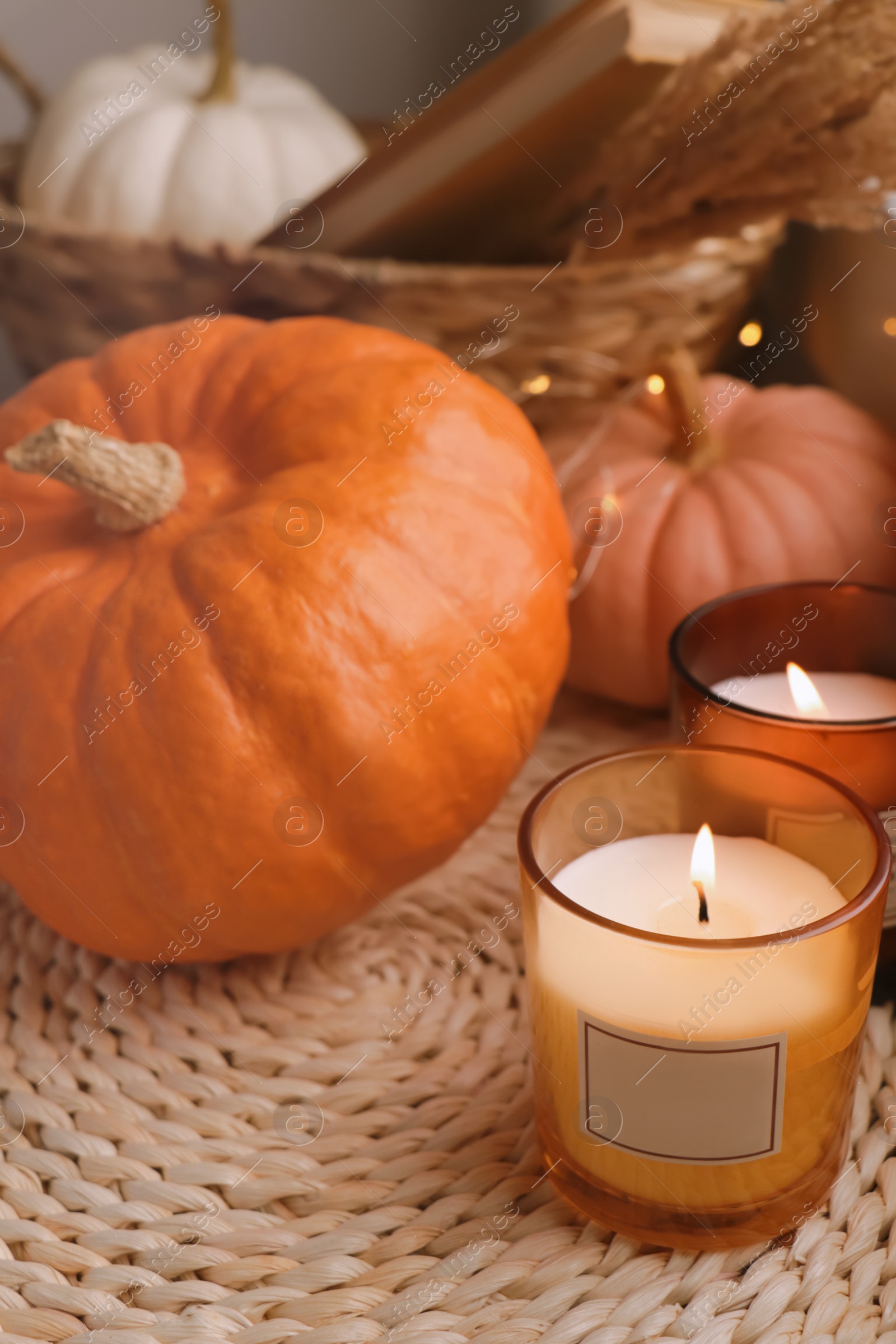 Photo of Scented candles and pumpkins on wicker mat indoors