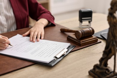 Photo of Notary signing document at wooden table in office, closeup