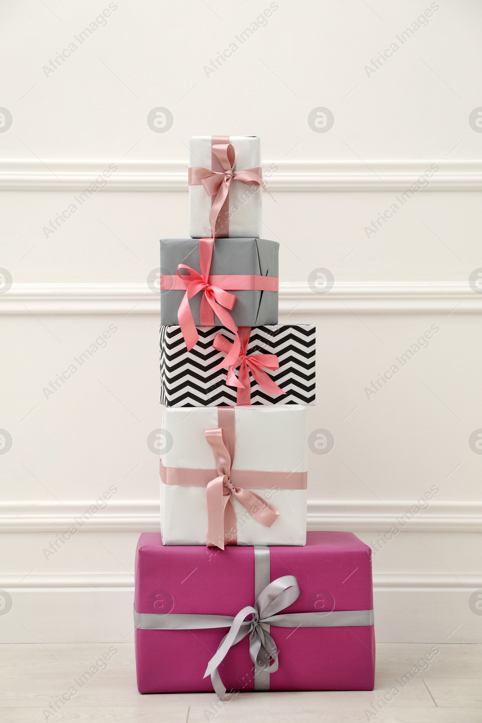 Photo of Many gift boxes with colorful bows near white wall