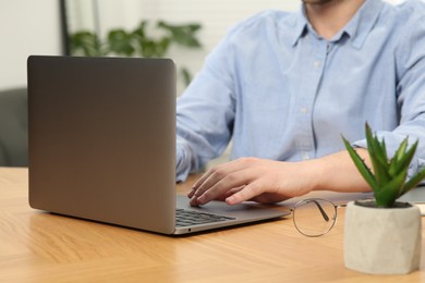 Photo of Man working with laptop at wooden table indoors, closeup