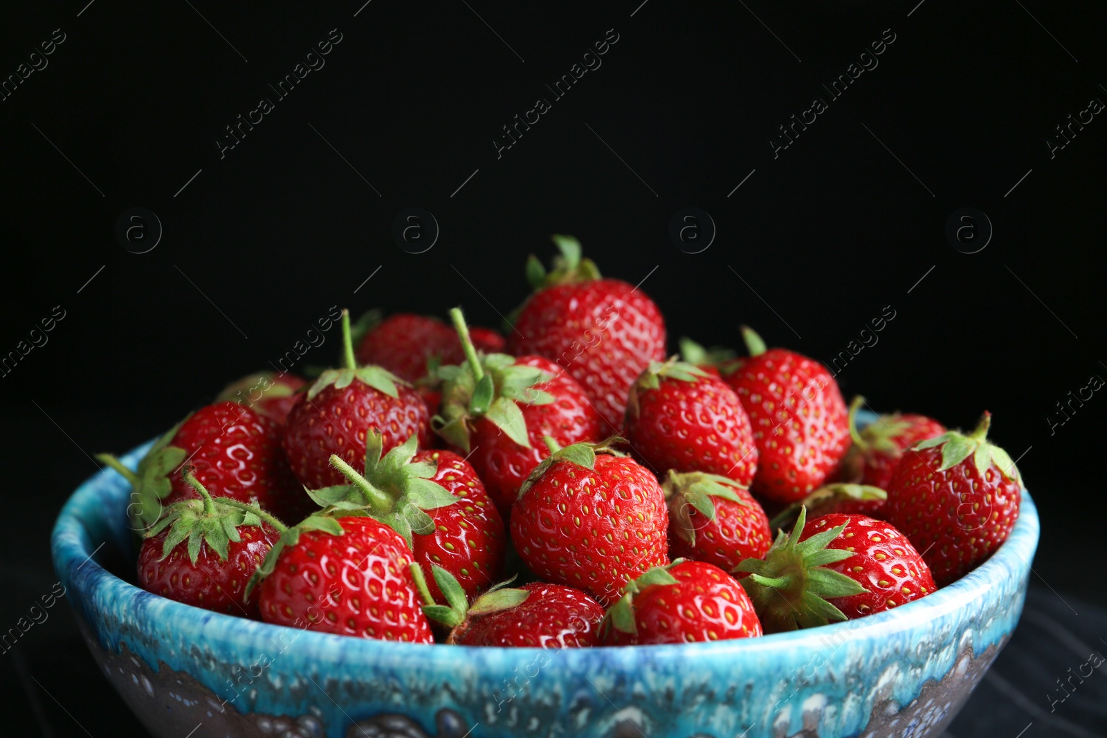 Photo of Delicious ripe strawberries in bowl on black background, closeup