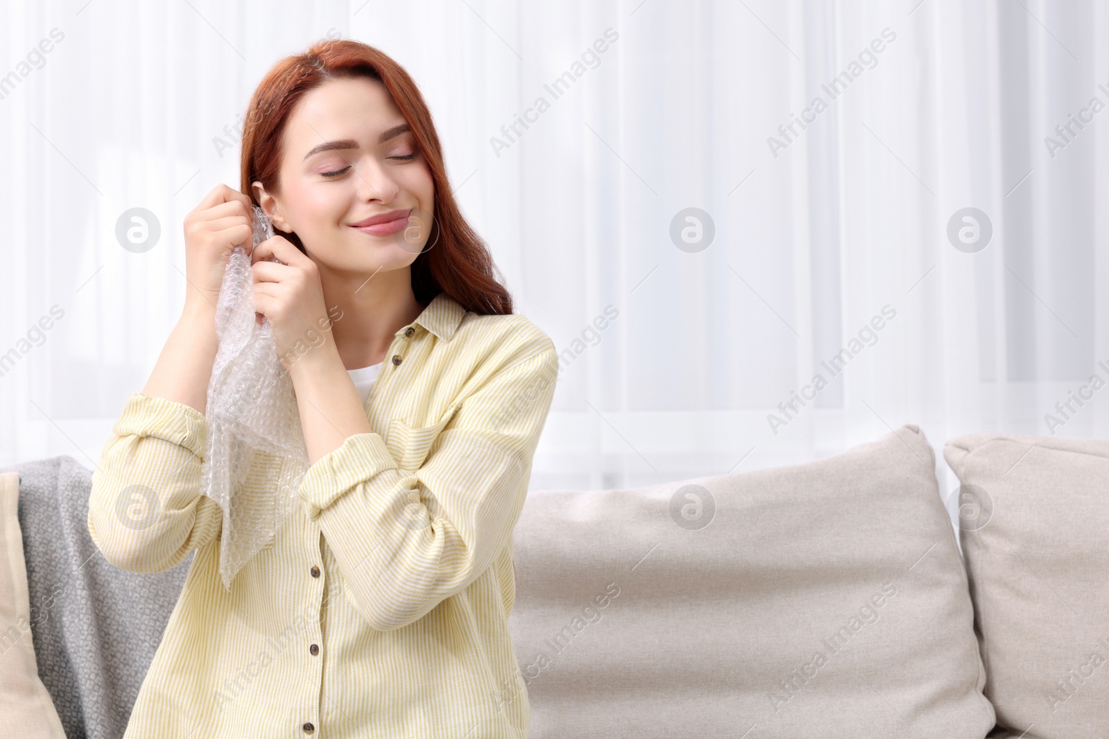 Photo of Woman popping bubble wrap on sofa at home, space for text. Stress relief