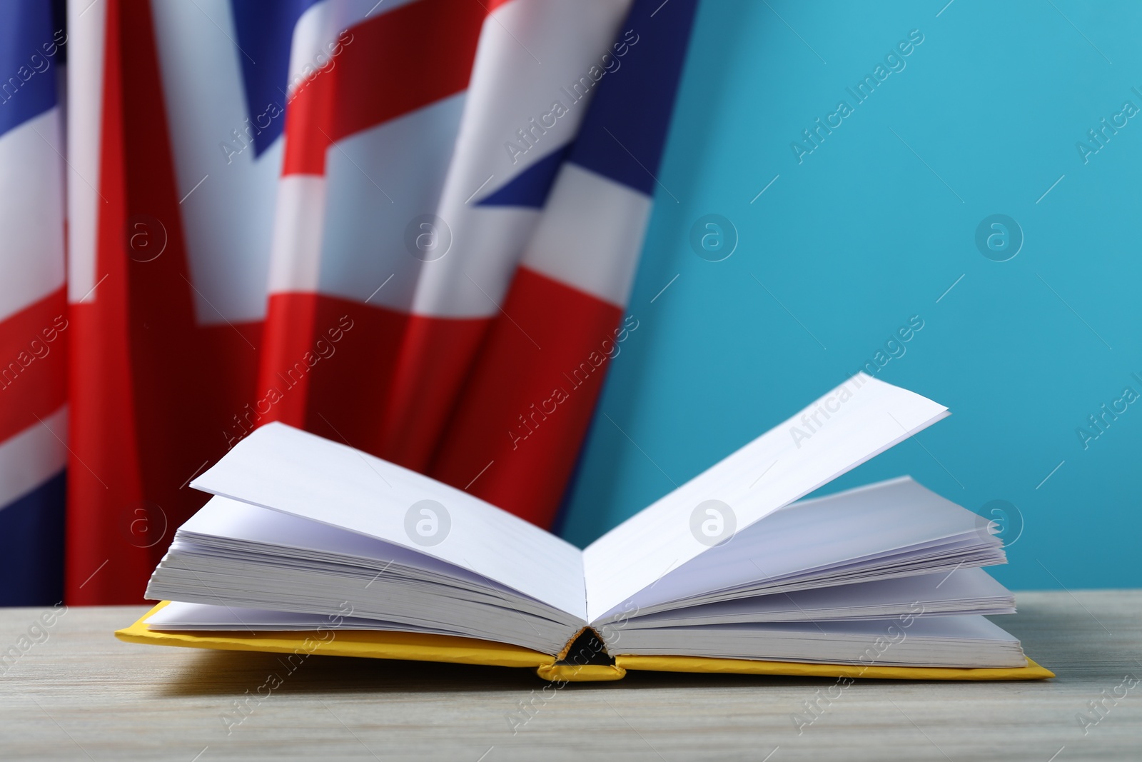 Photo of Learning foreign language. Open book on wooden table near flag of United Kingdom, space for text