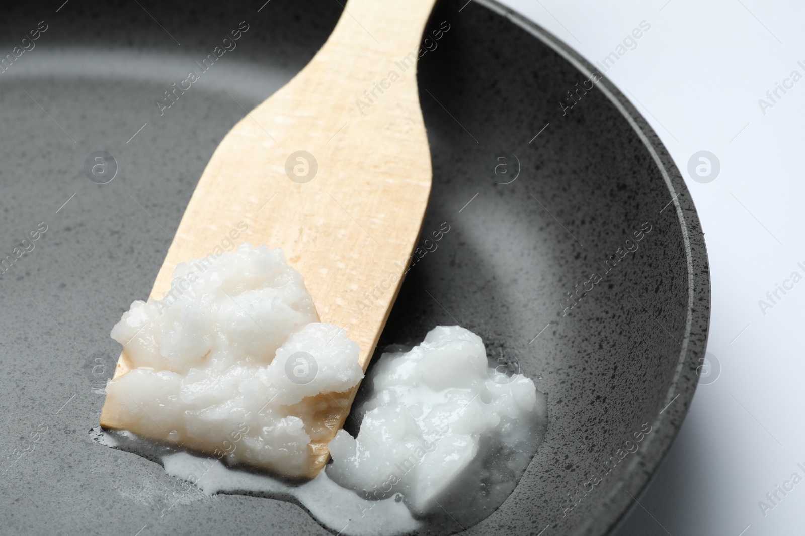 Photo of Frying pan with coconut oil and wooden spatula on white background, closeup. Healthy cooking