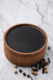 Photo of Wooden bowl with balsamic vinegar and peppercorns on white textured table, closeup