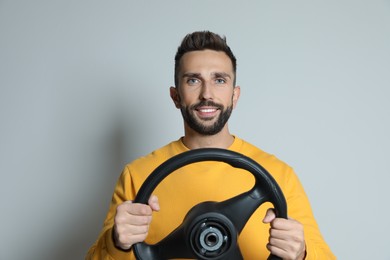 Photo of Happy man with steering wheel on grey background