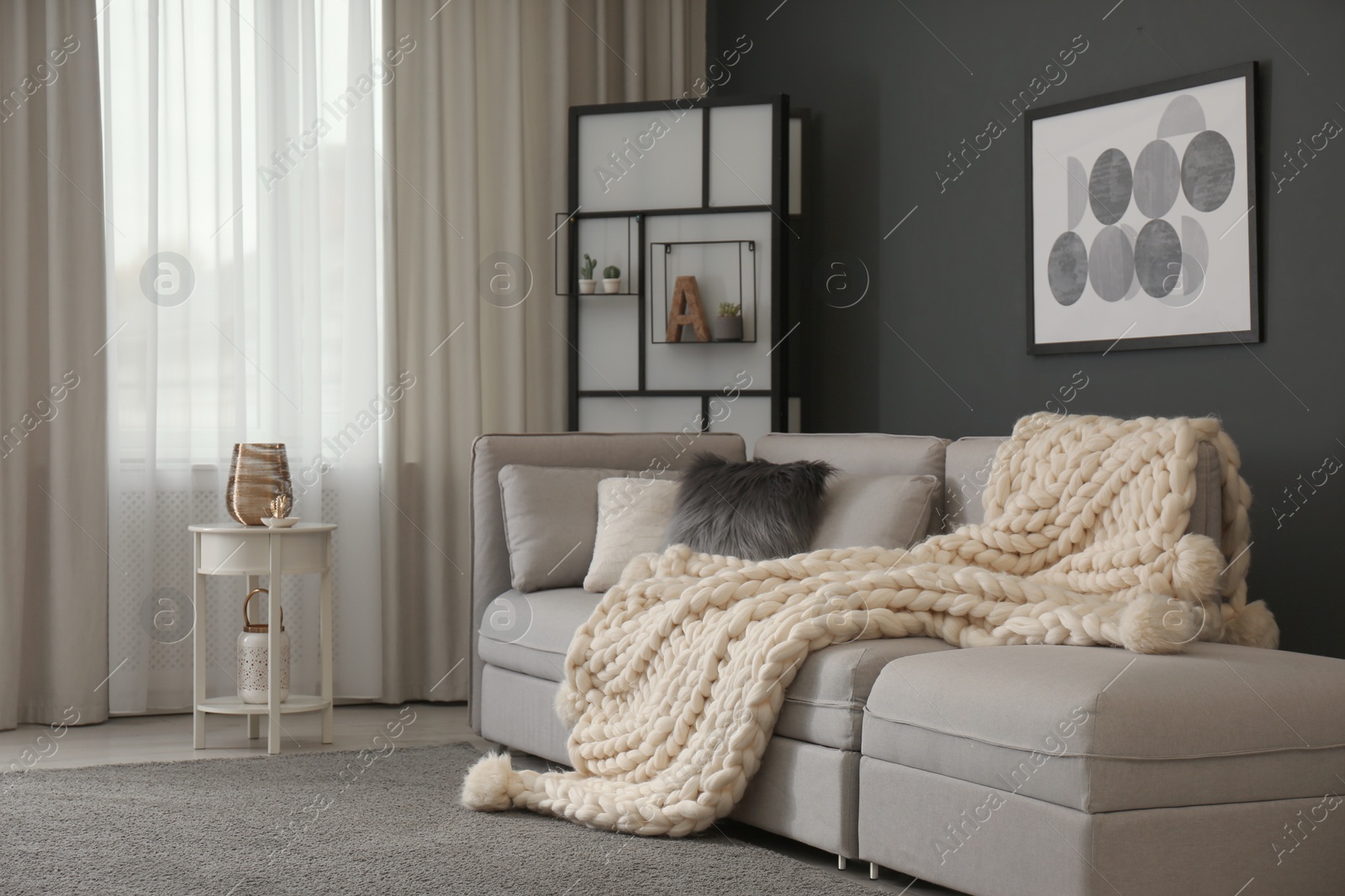 Photo of Comfortable sofa with knitted plaid in living room. Interior design