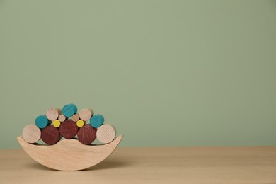 Photo of Wooden balance toy on table near olive wall, space for text. Children's development