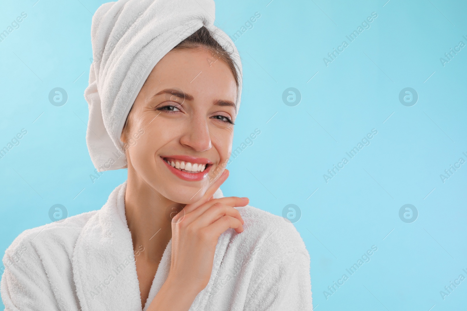 Photo of Beautiful young woman with hair wrapped in towel after washing on light blue background. Space for text