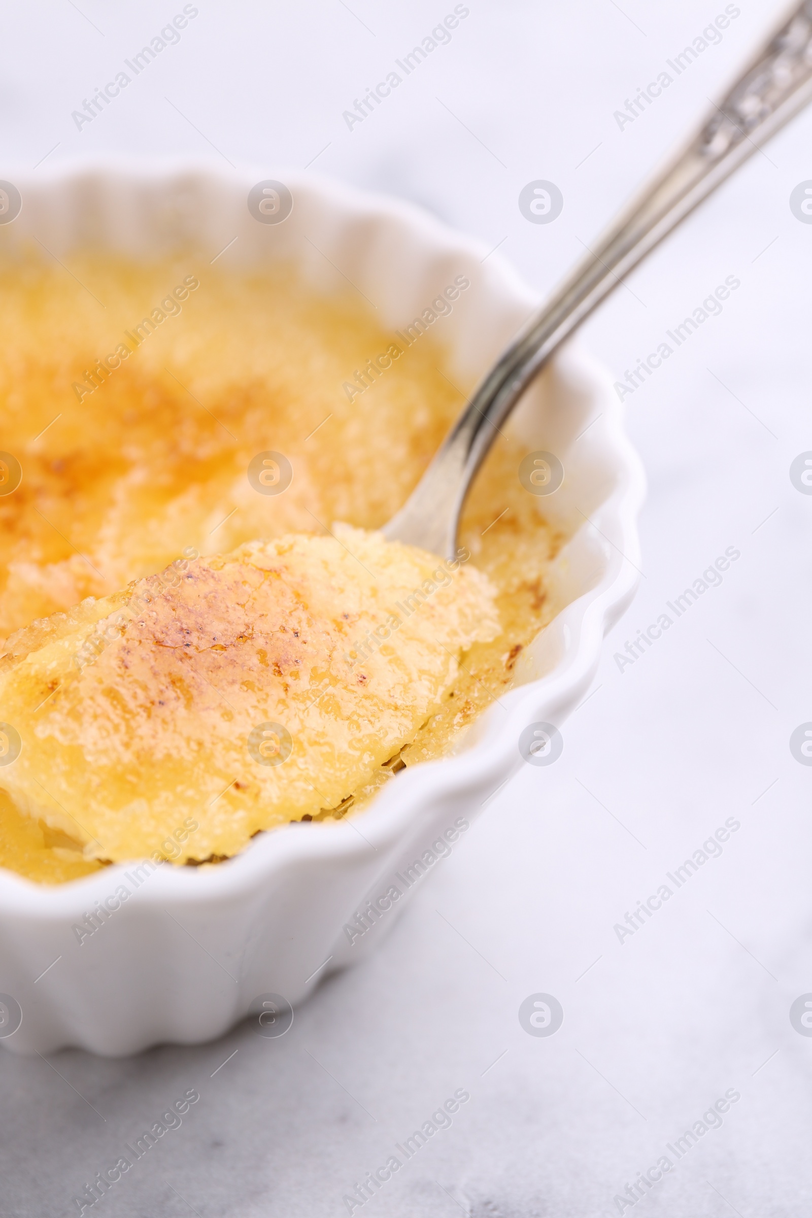 Photo of Eating delicious creme brulee at white table, closeup