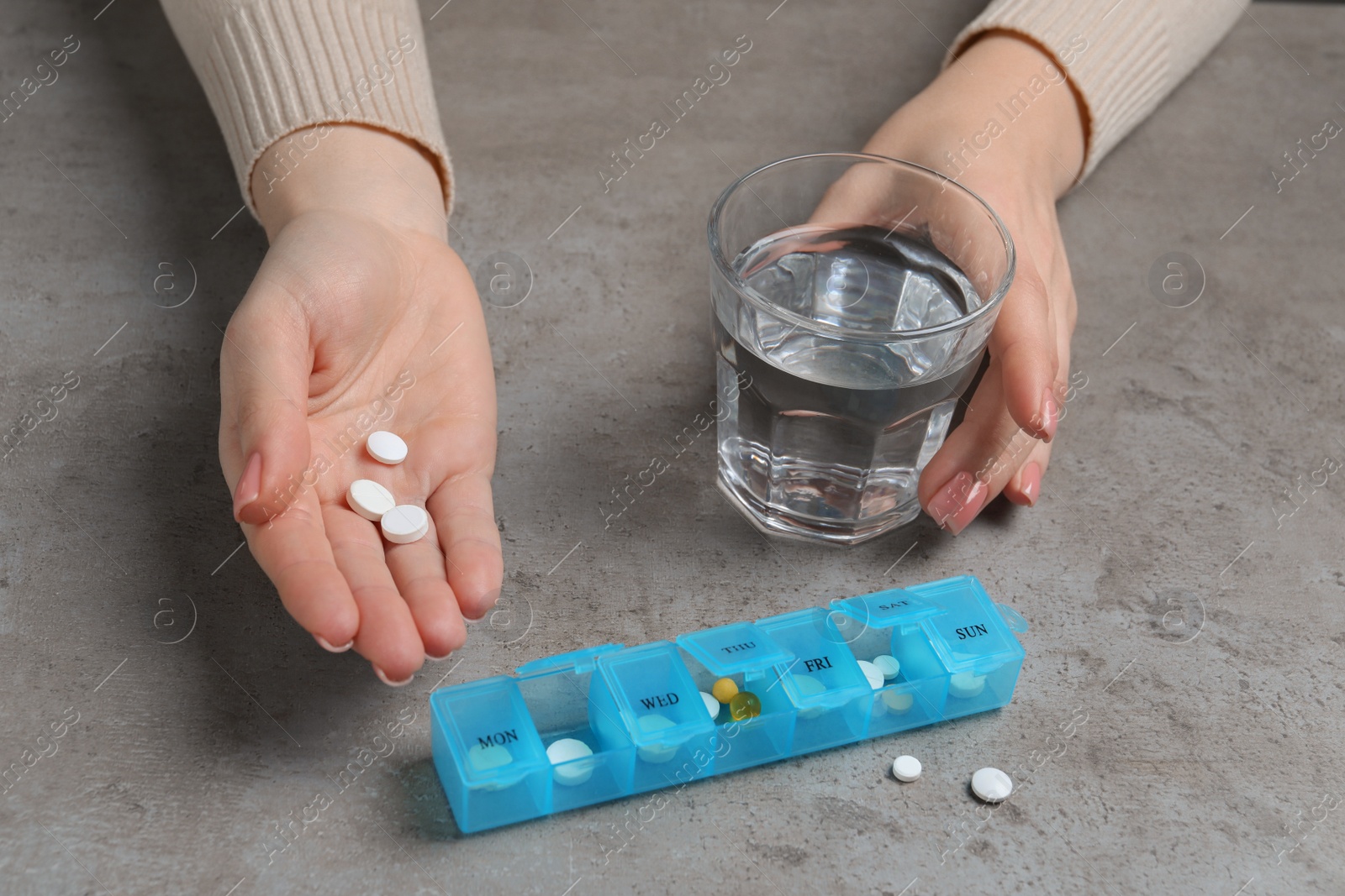 Photo of Woman holding glass of water and pills at grey table, closeup