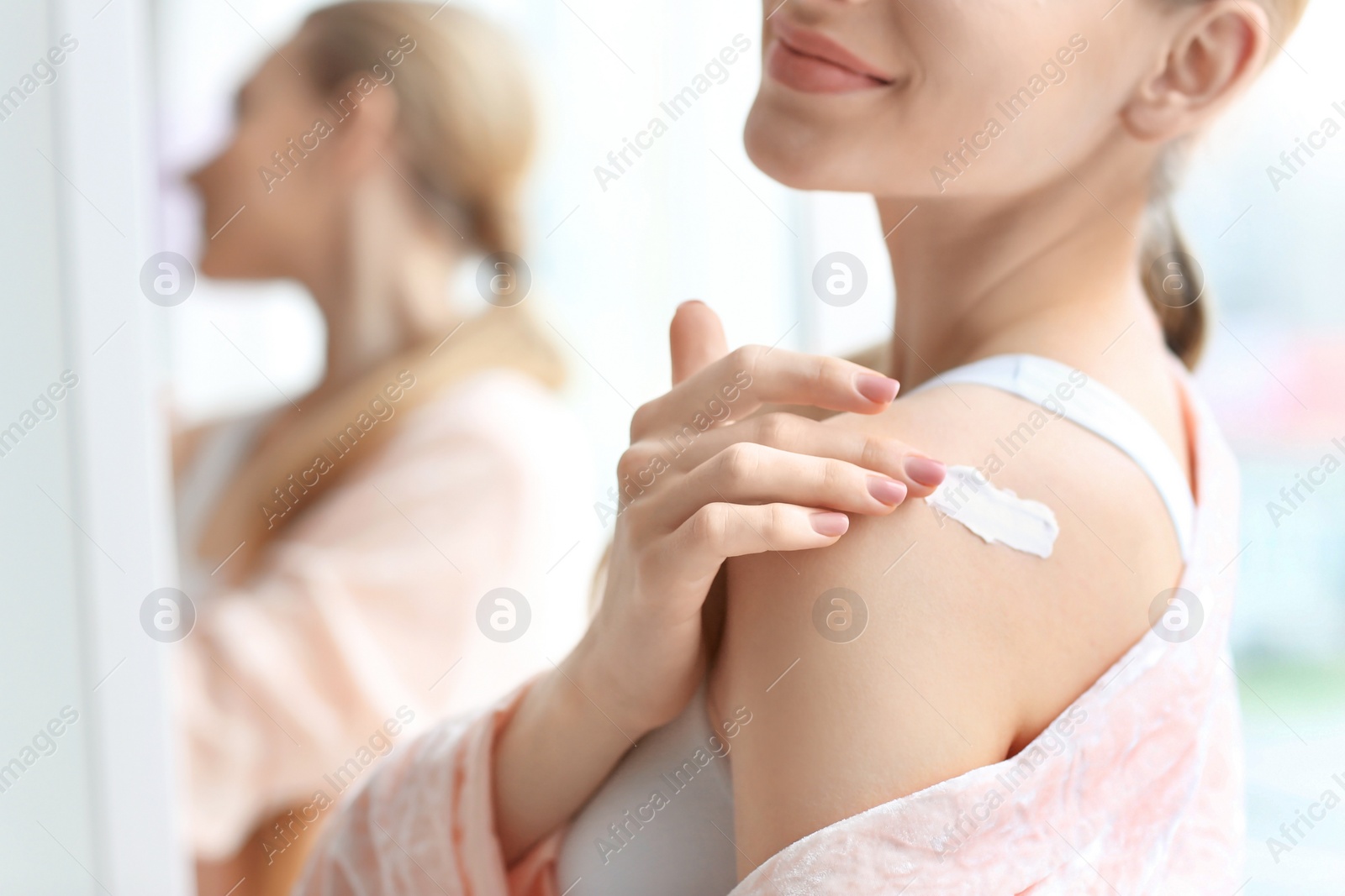 Photo of Young woman applying body cream at home