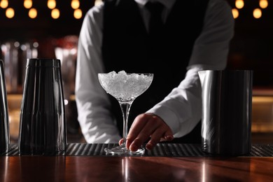 Photo of Bartender preparing fresh alcoholic cocktail in martini glass at bar counter, closeup