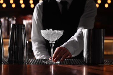 Bartender preparing fresh alcoholic cocktail in martini glass at bar counter, closeup