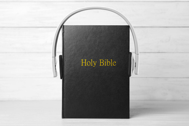 Photo of Bible and headphones on table against white wooden background. Religious audiobook