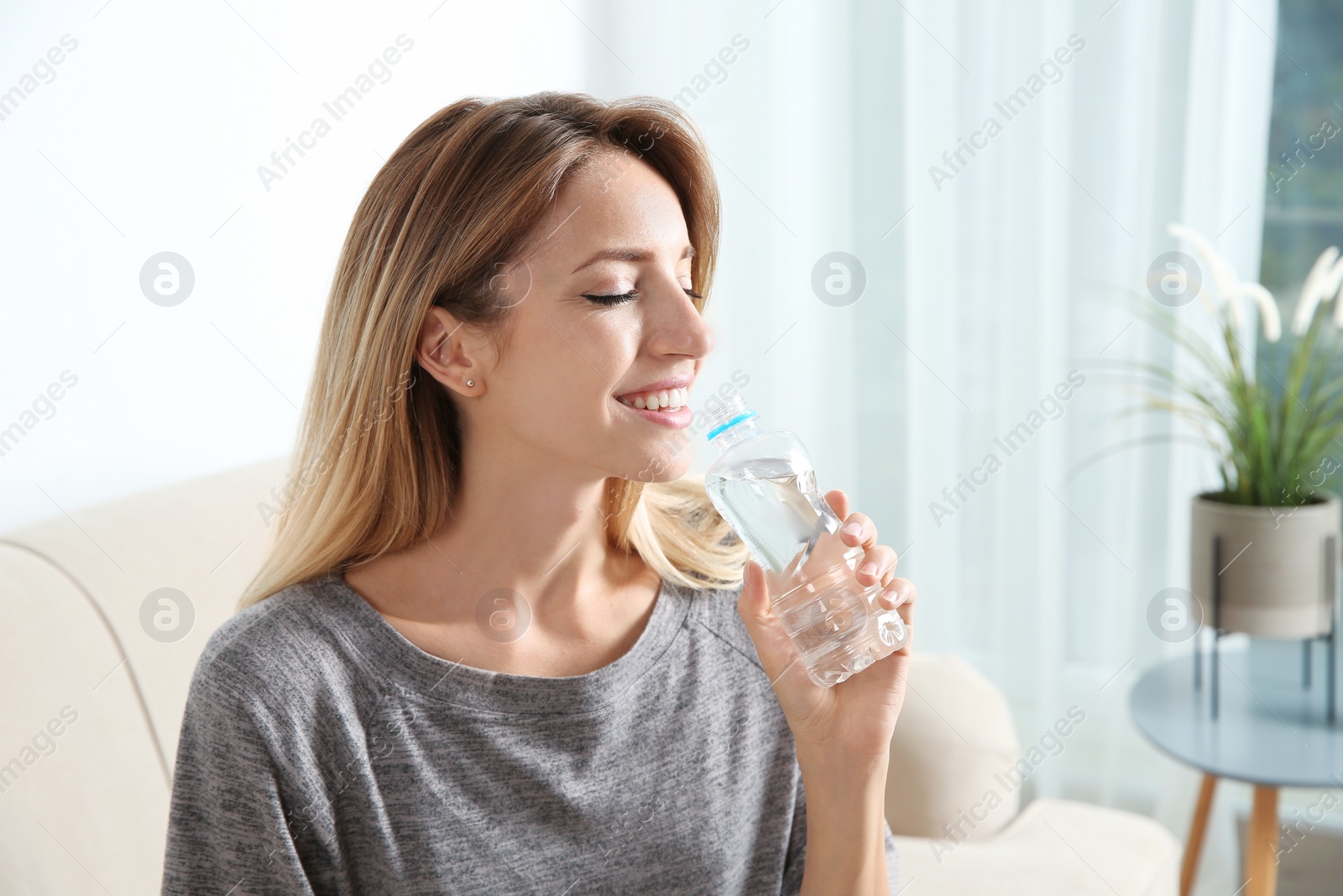 Photo of Young woman drinking water from bottle at home