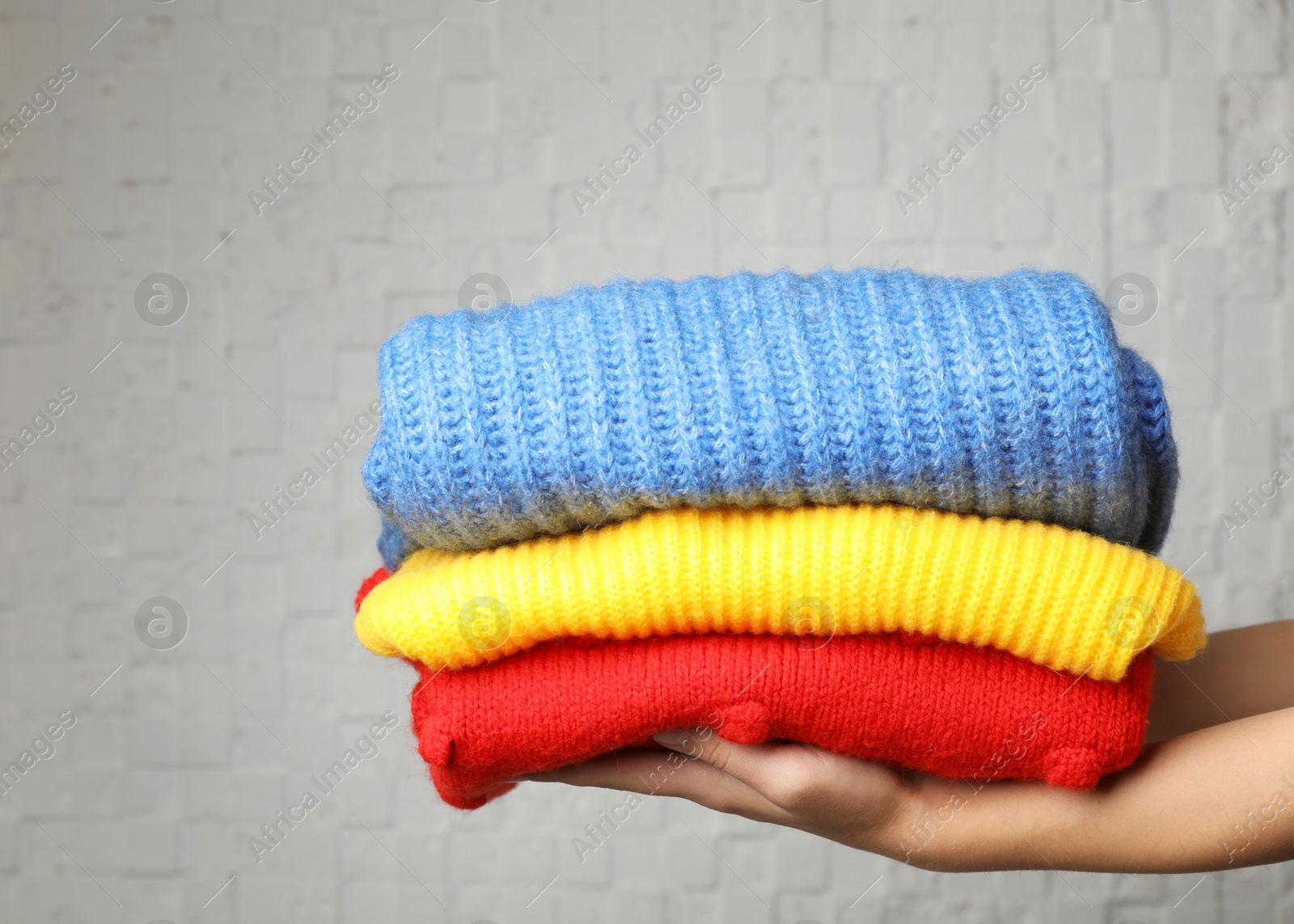 Photo of Woman holding stack of folded warm knitted sweaters against brick wall