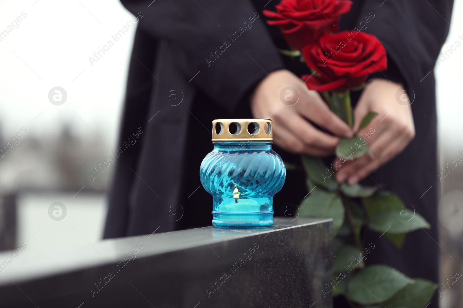 Photo of Woman with red roses outdoors, focus on candle. Funeral ceremony