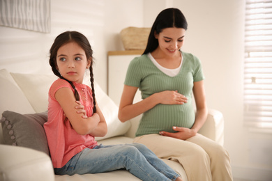 Unhappy little girl near pregnant mother at home. Feeling jealous towards unborn sibling