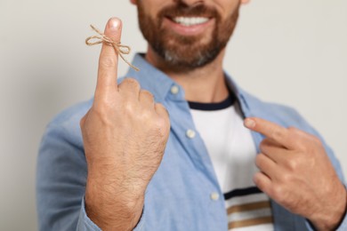 Smiling man showing index finger with tied bow as reminder against light grey background, focus on hand