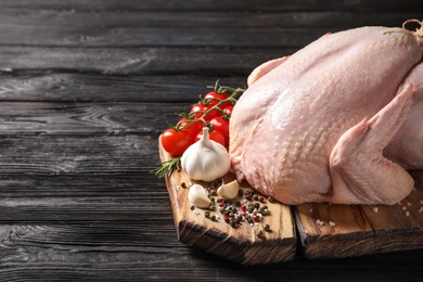 Photo of Board with raw turkey and ingredients on wooden background. Space for text