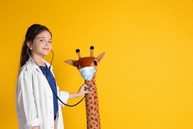 Little girl playing doctor with toy giraffe on yellow background, space for text. Pediatrician practice