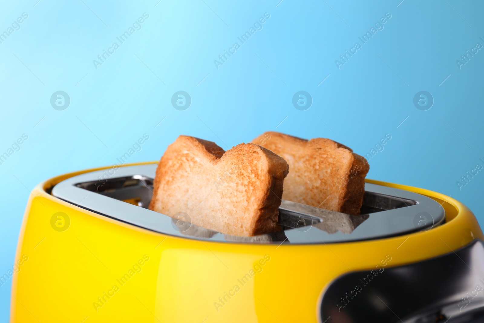 Photo of Yellow toaster with roasted bread against light blue background, closeup