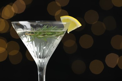 Martini glass of refreshing cocktail with lemon slice and rosemary against blurred lights, space for text