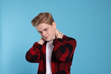Photo of Teenage boy suffering from pain in neck on light blue background. Arthritis symptom