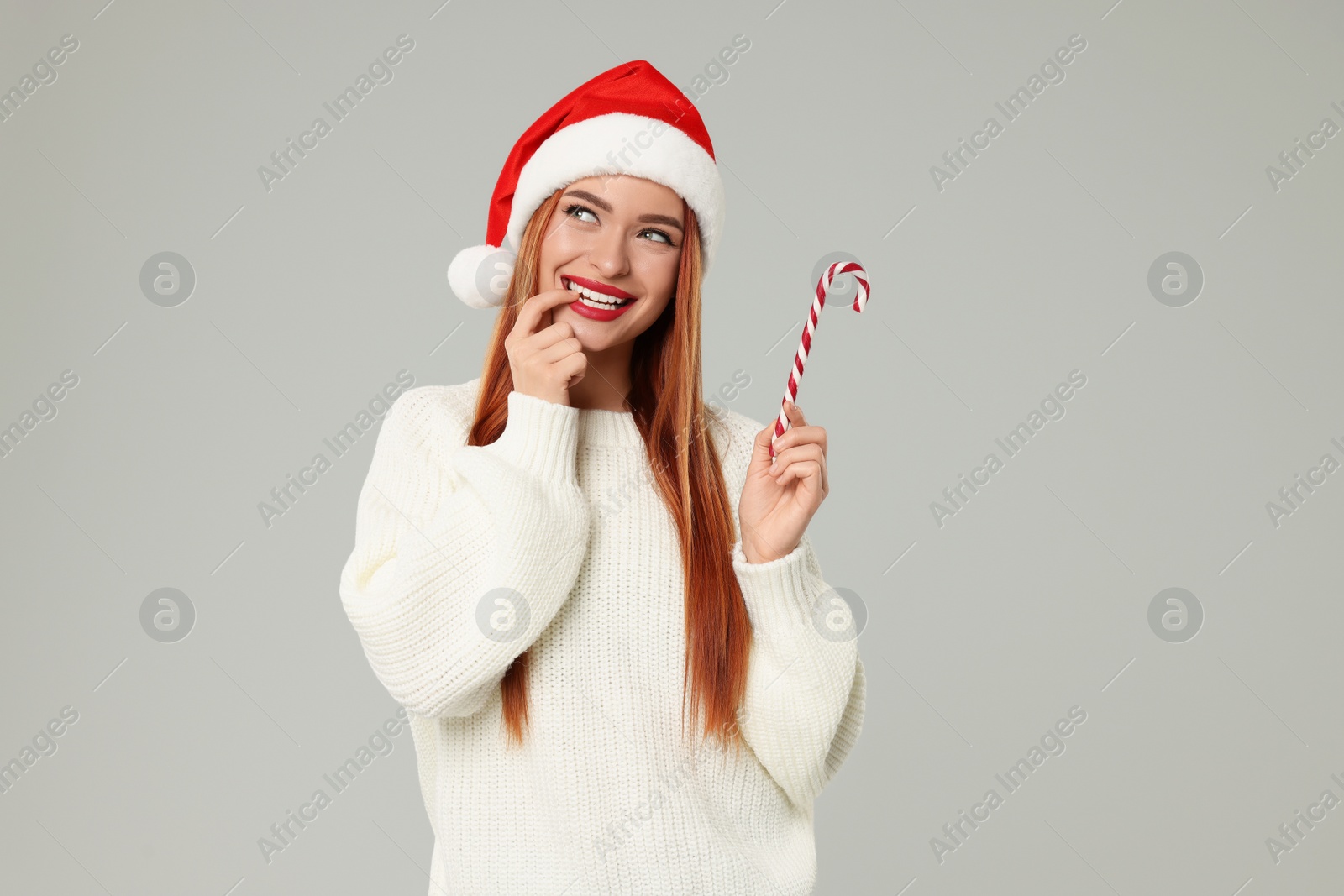 Photo of Young woman in Santa hat with candy cane on light grey background. Christmas celebration