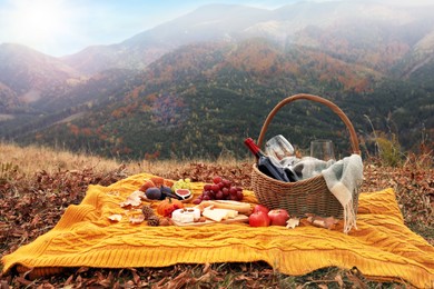 Image of Knitted plaid with picnic basket, wine and snacks in mountains on autumn day