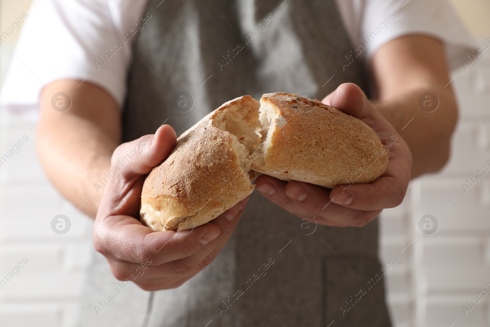 Photo of Man breaking loaf of fresh bread near white brick wall, closeup