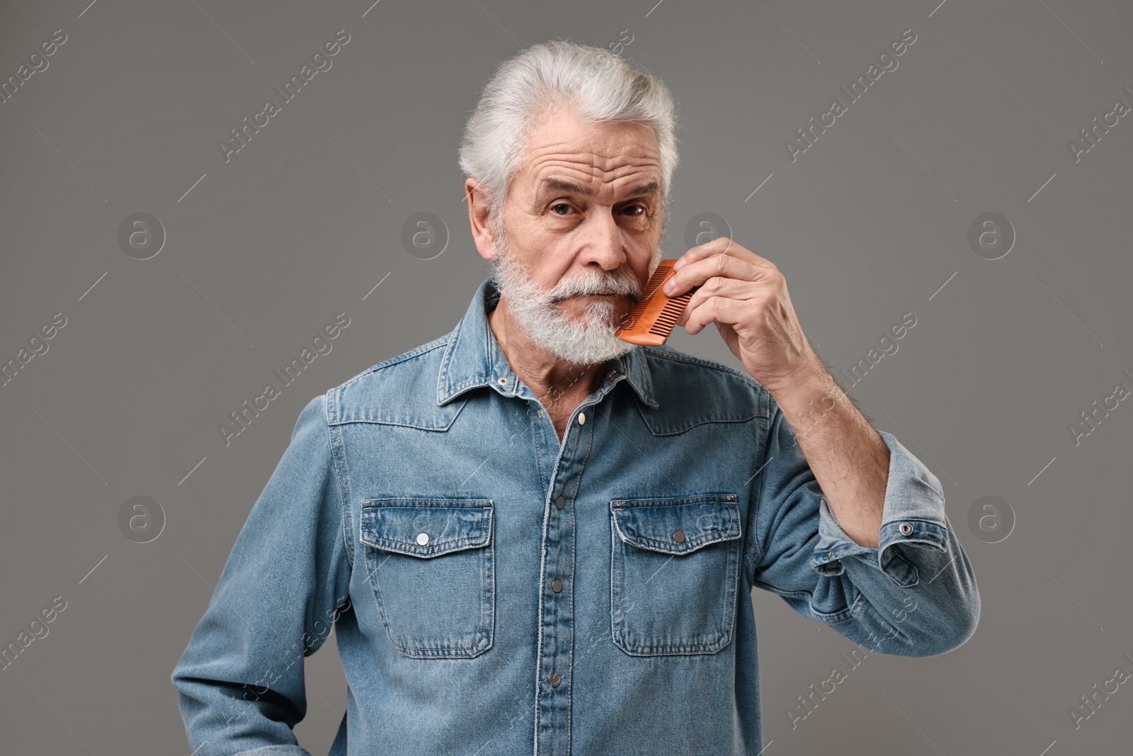 Photo of Senior man combing beard on grey background