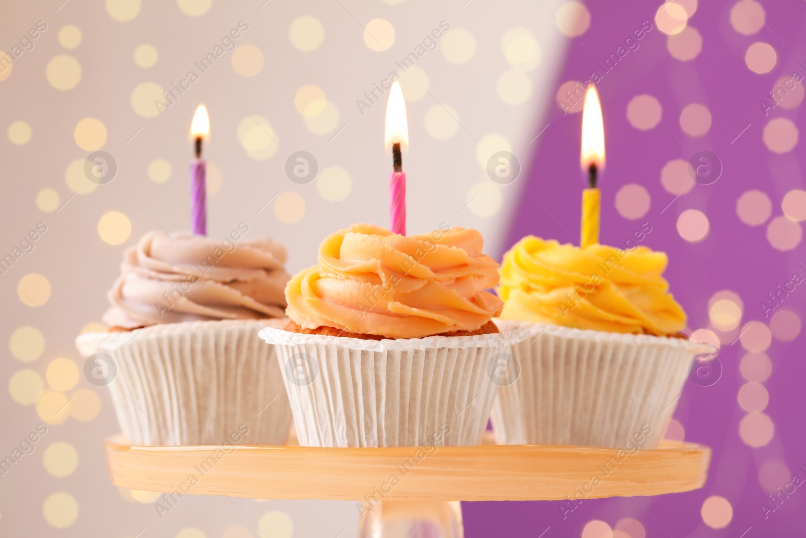 Photo of Tasty birthday cupcakes with candles on stand against blurred lights, closeup