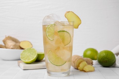 Photo of Glass of tasty ginger ale with ice cubes and ingredients on white tiled table