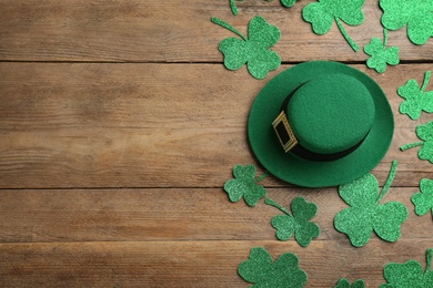 Photo of Leprechaun's hat and decorative clover leaves on wooden background, flat lay with space for text. St. Patrick's day celebration