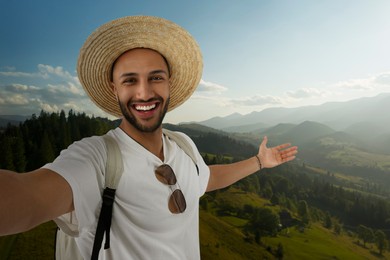 Smiling young man in straw hat taking selfie in mountains