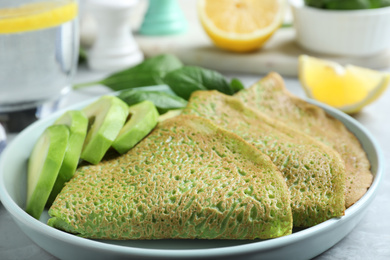 Delicious spinach crepes with avocado on table, closeup