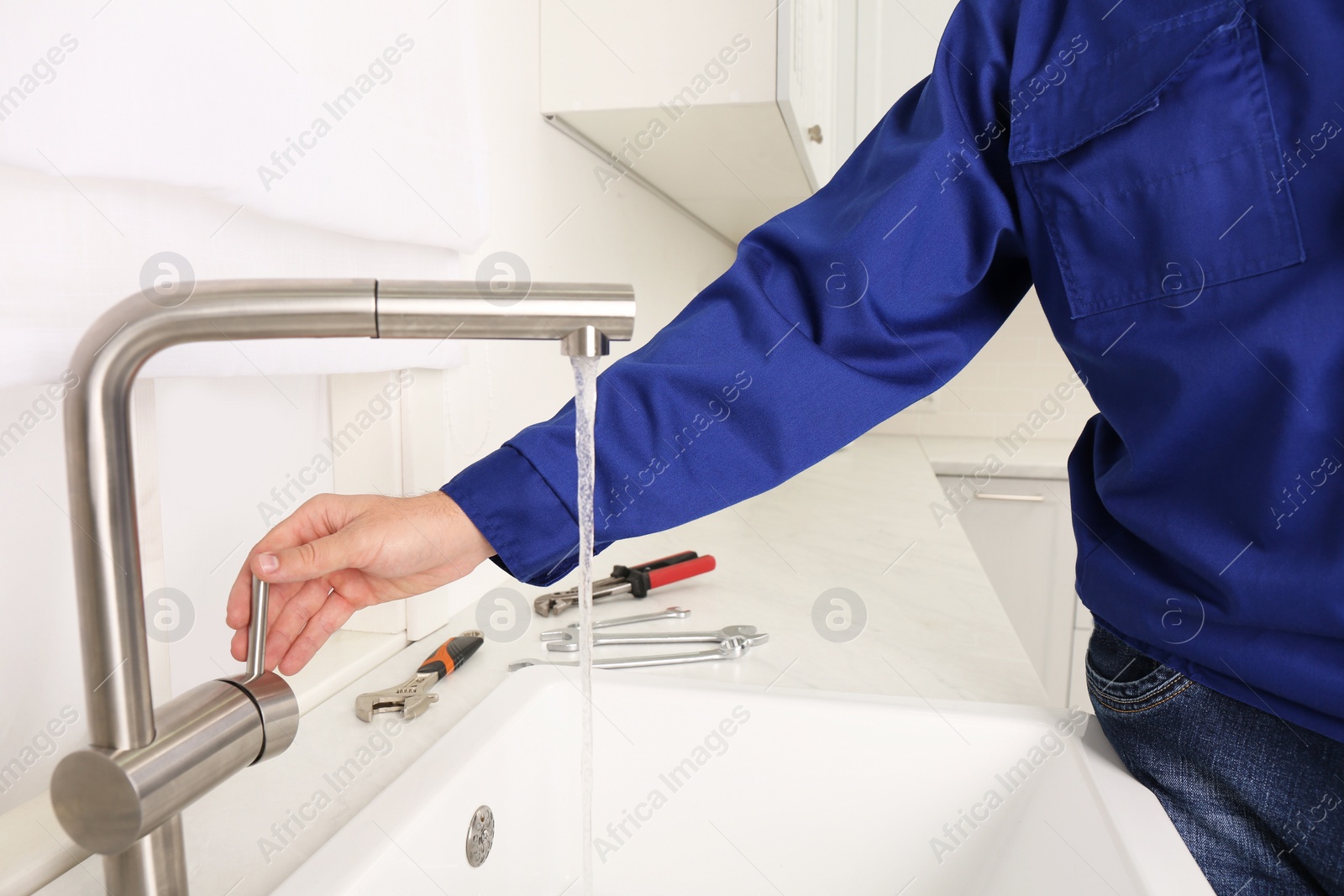 Photo of Plumber checking water flow from tap in kitchen, closeup. Repair service