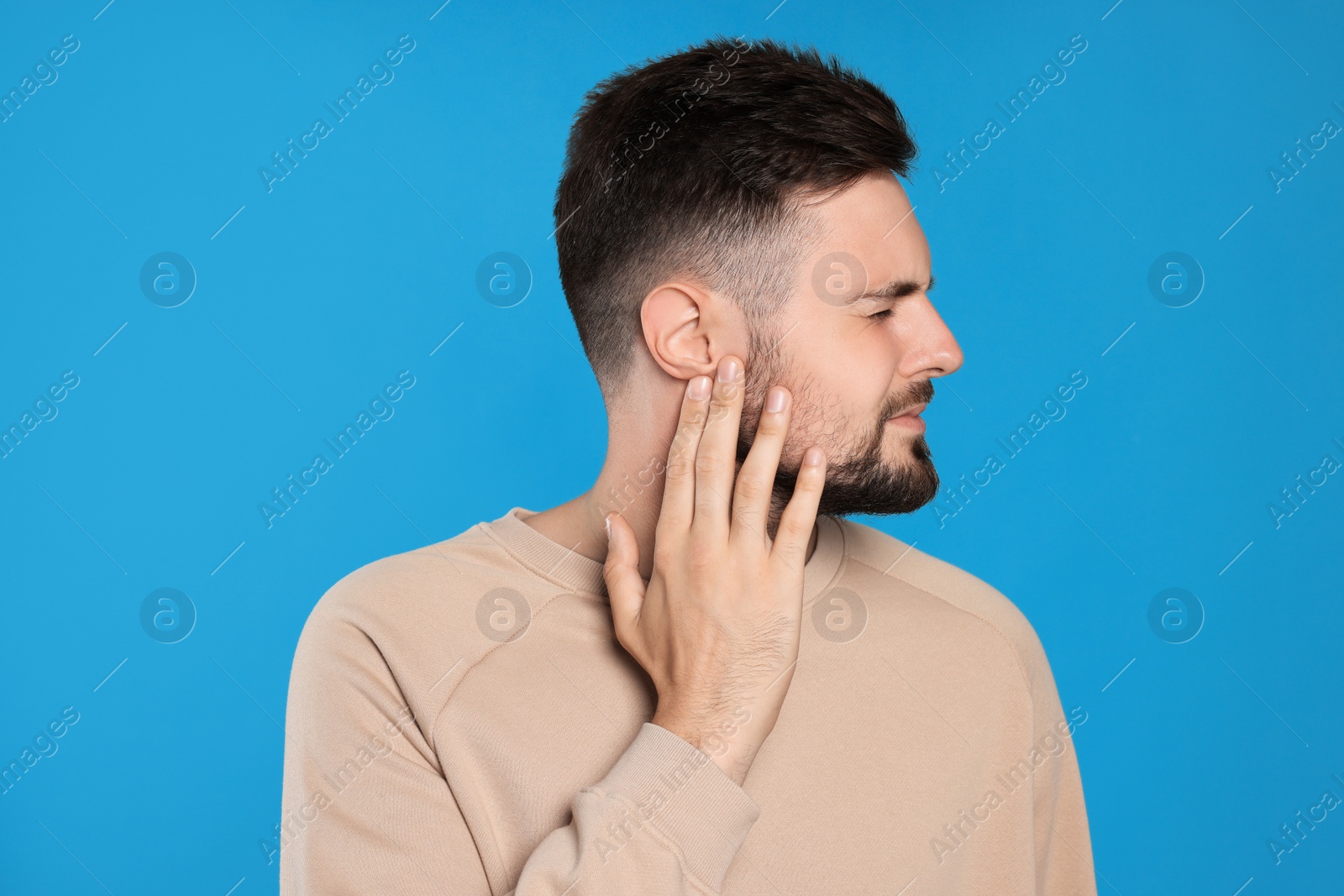 Photo of Young man suffering from ear pain on light blue background