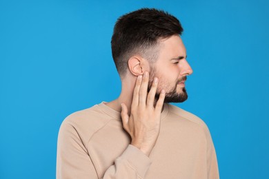 Photo of Young man suffering from ear pain on light blue background