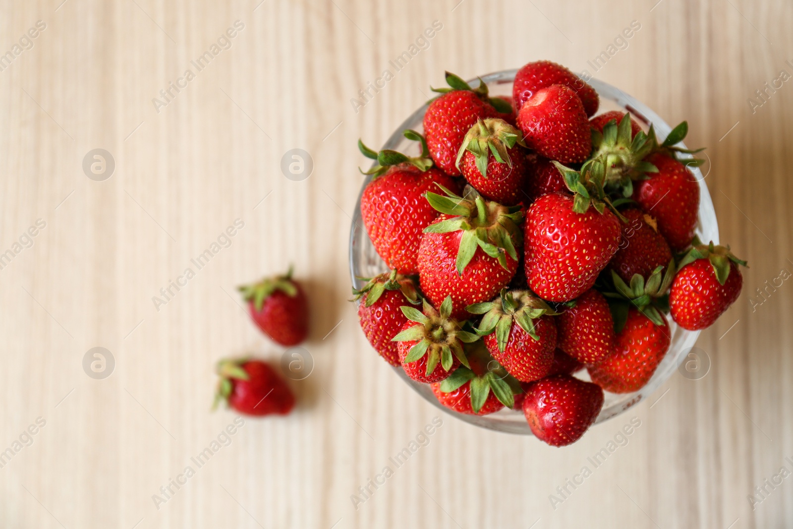 Photo of Glass bowl with ripe strawberries on white wooden table, top view. Space for text