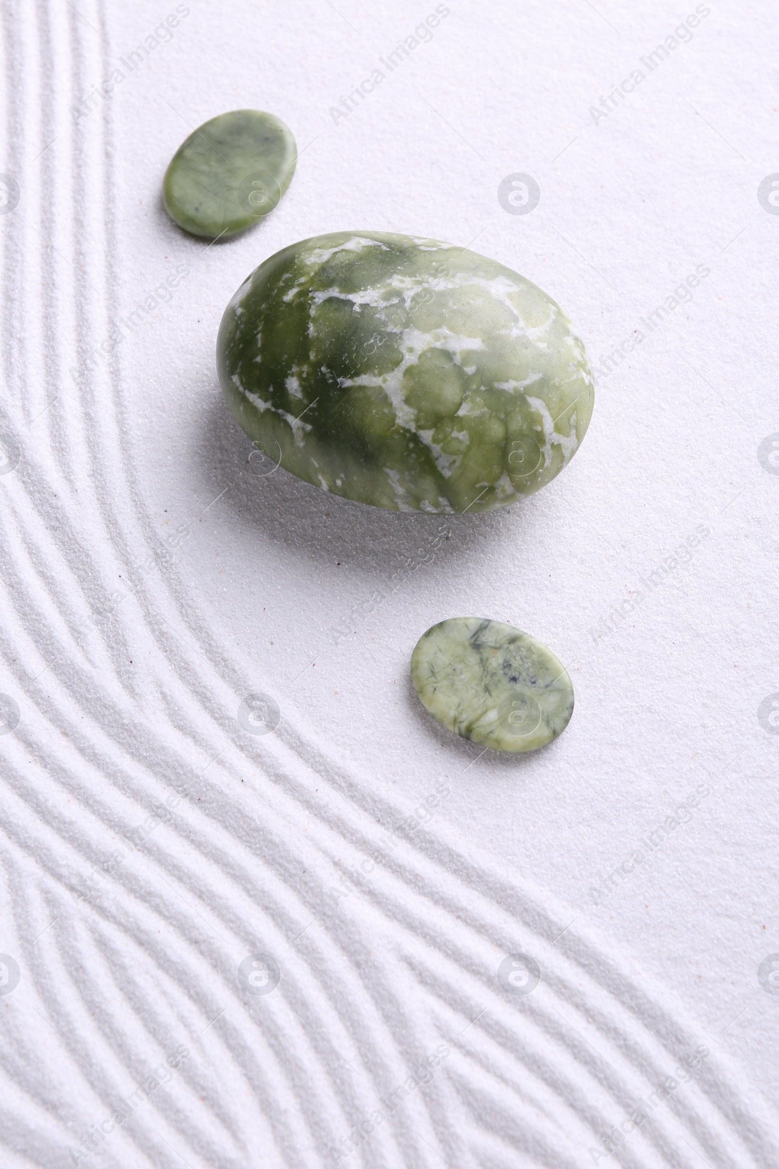 Photo of Zen garden stones on white sand with pattern, flat lay