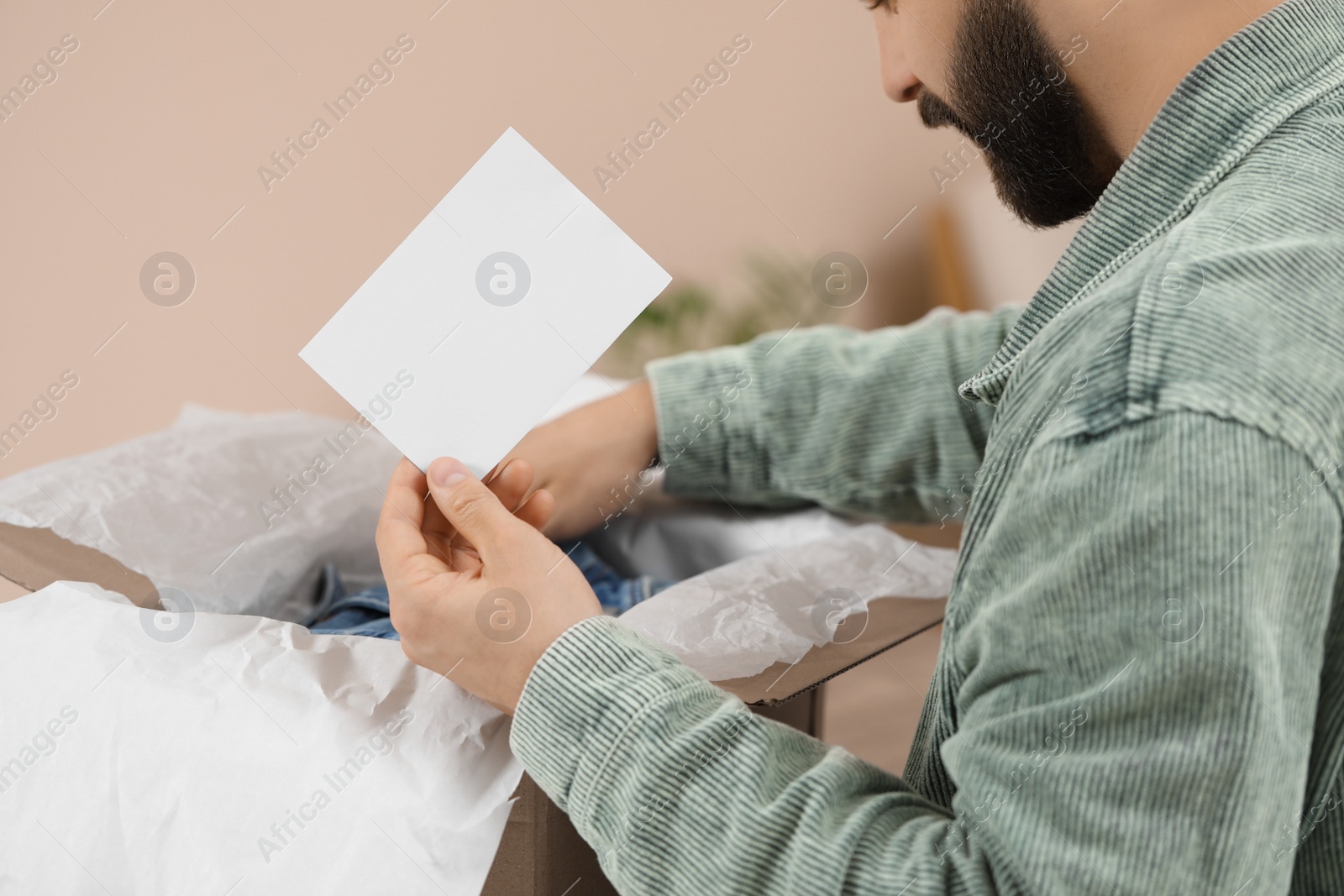 Photo of Man holding greeting card near parcel with Christmas gift at home, closeup